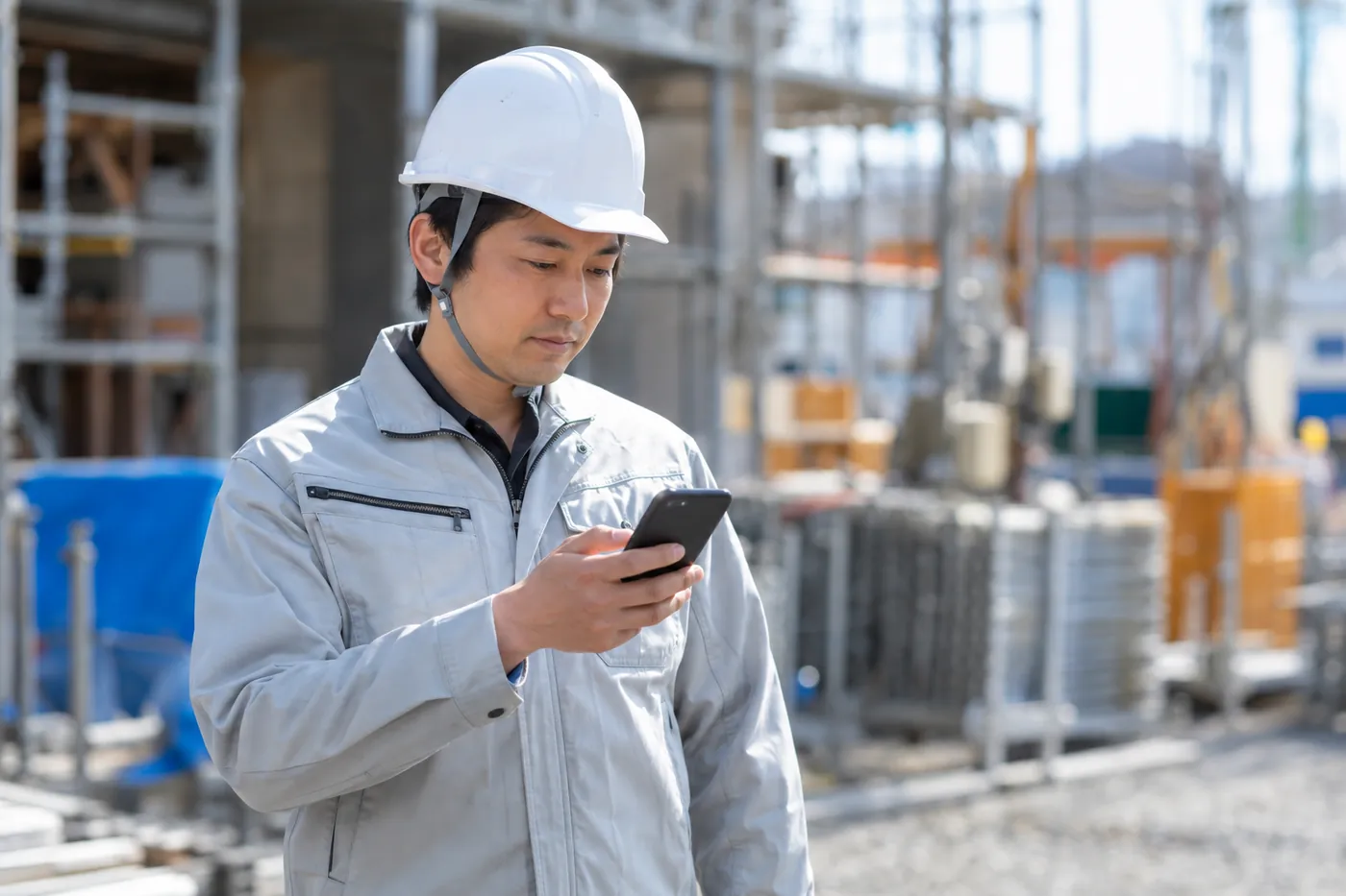 工事現場でスマートフォンから見積を作成するヘルメット姿の担当者